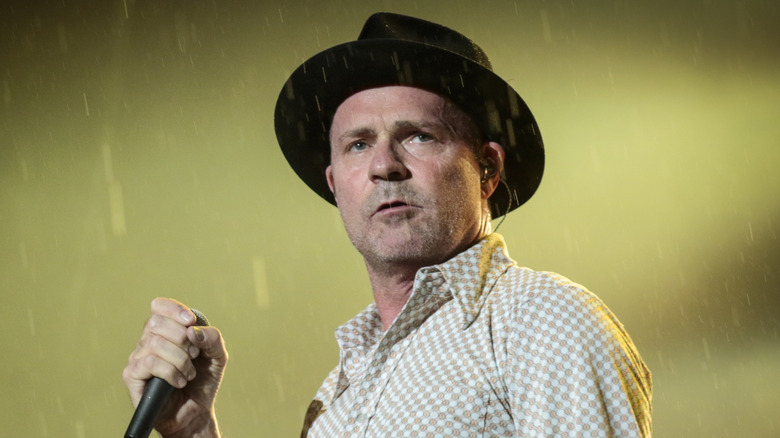 Gord Downie wearing hat and holding a mic on stage in rain