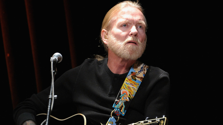 Gregg Allman sat playing guitar in dark shirt