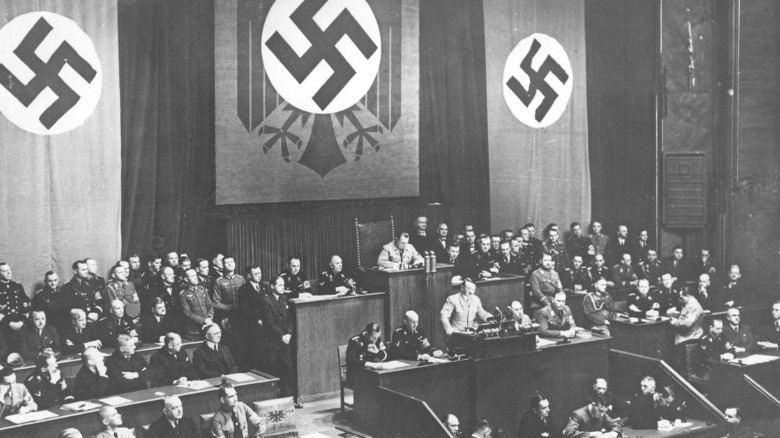 Hitler speaking with swastikas in background