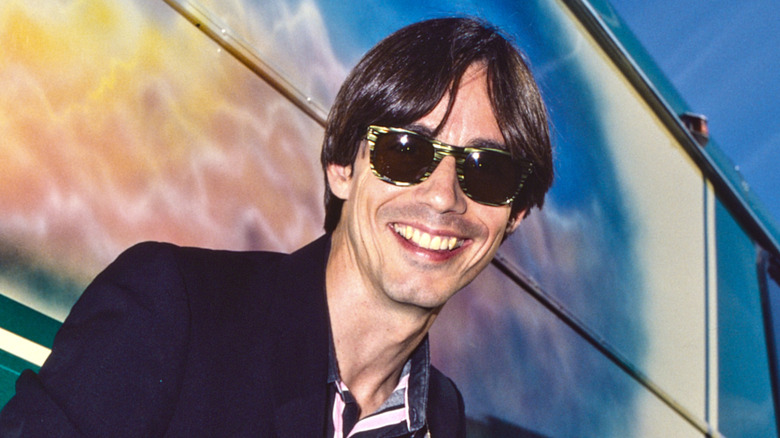 Jackson Browne smiling in sunglasses in the 1970s by a tour bus