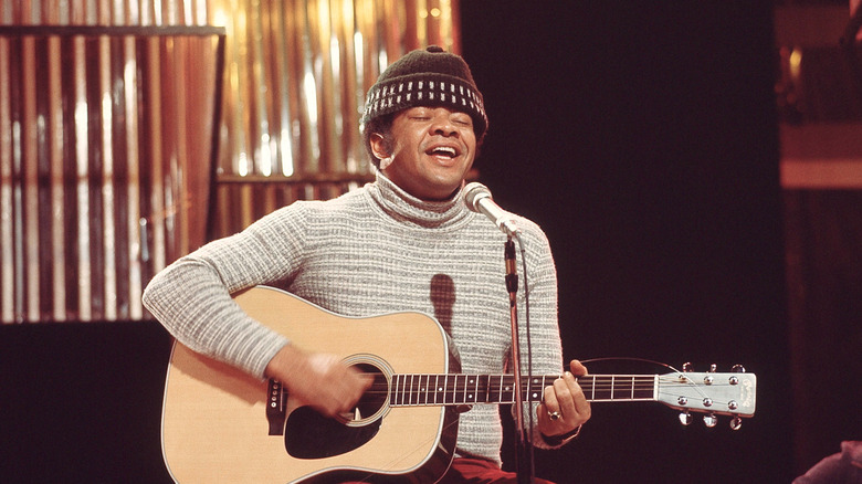 Bill Withers singing and playing guitar with eyes closed