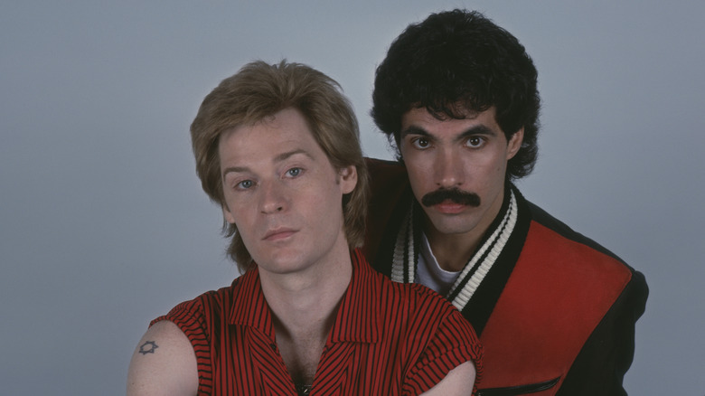 Daryl Hall and John Oates posing for a photo in front of a grey background