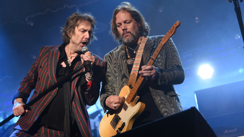 Chris Robinson singing into a microphone next to Rich Robinson playing guitar
