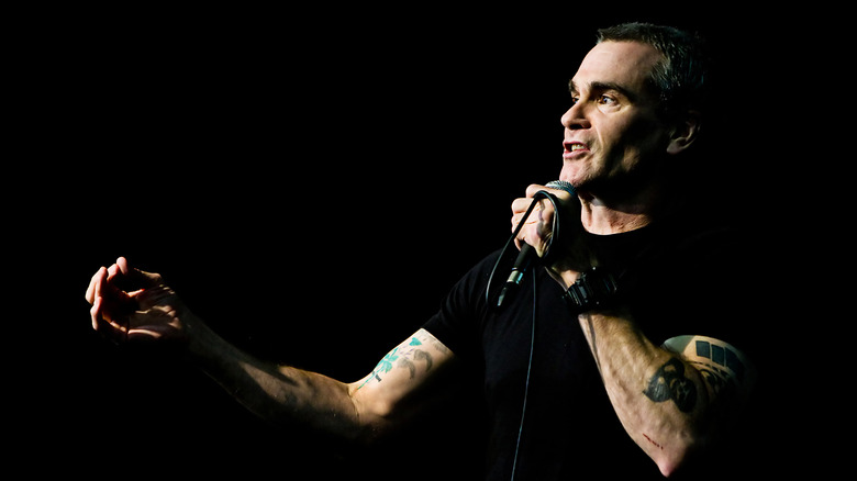 Henry Rollins in black shirt performing on dark stage