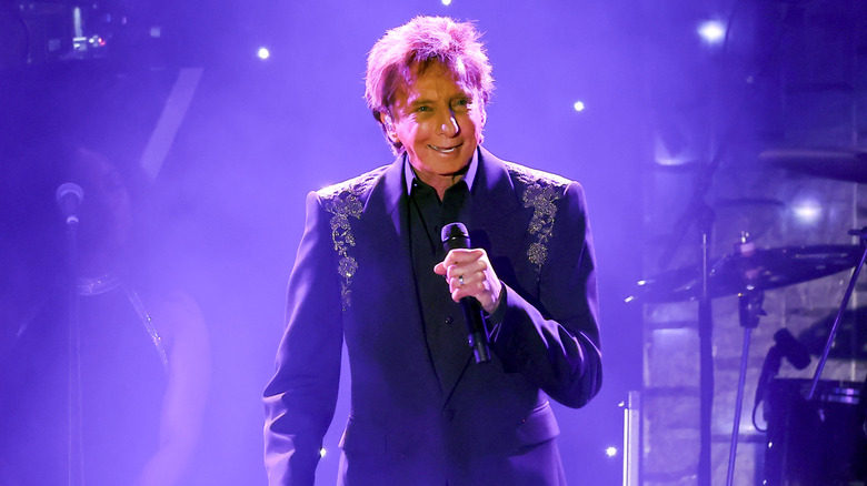 Barry Manilow smiling in purple suit on stage in 2025