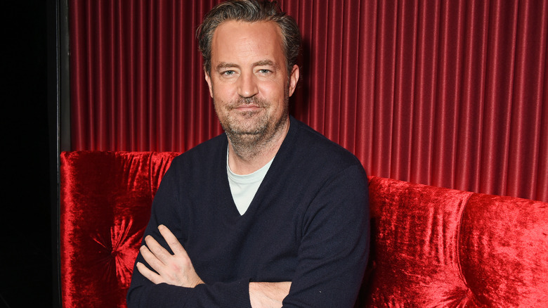 Matthew Perry sitting on a red sofa arms crossed