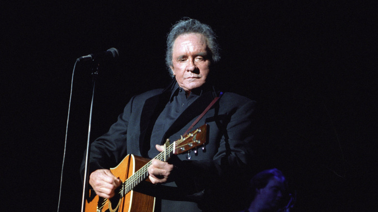 Johnny Cash in dark suit playing guitar on stage with black background