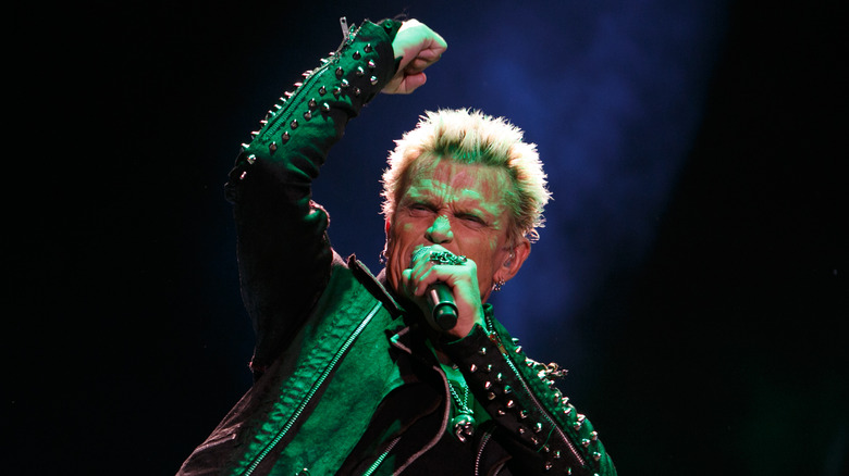 Billy Idol on stage singing holding mike leather jacket fist pumping