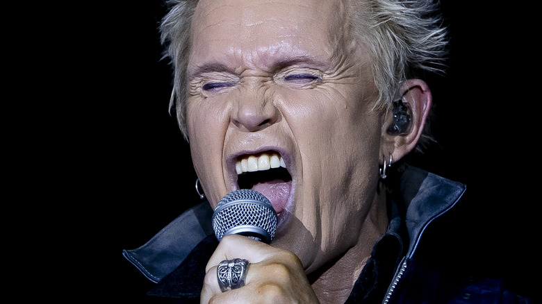 Billy Idol screaming into microphone dark background