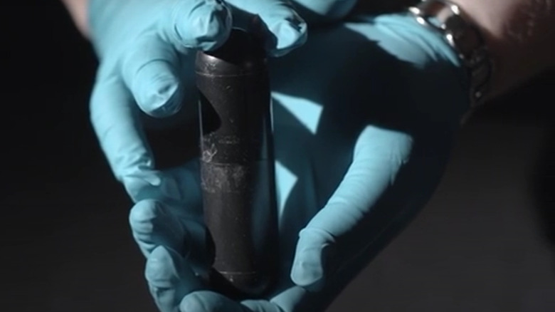 gloved hands holding metal capsule