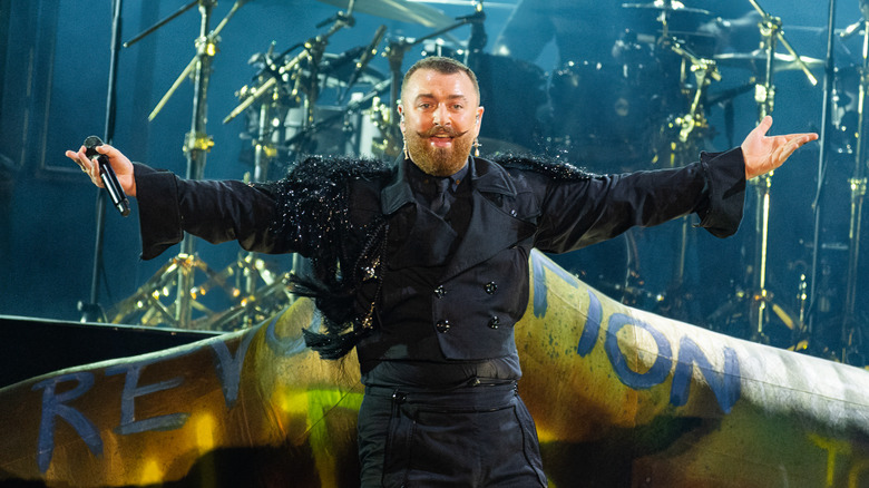 Sam Smith performing on stage with their arms spread open in 2024
