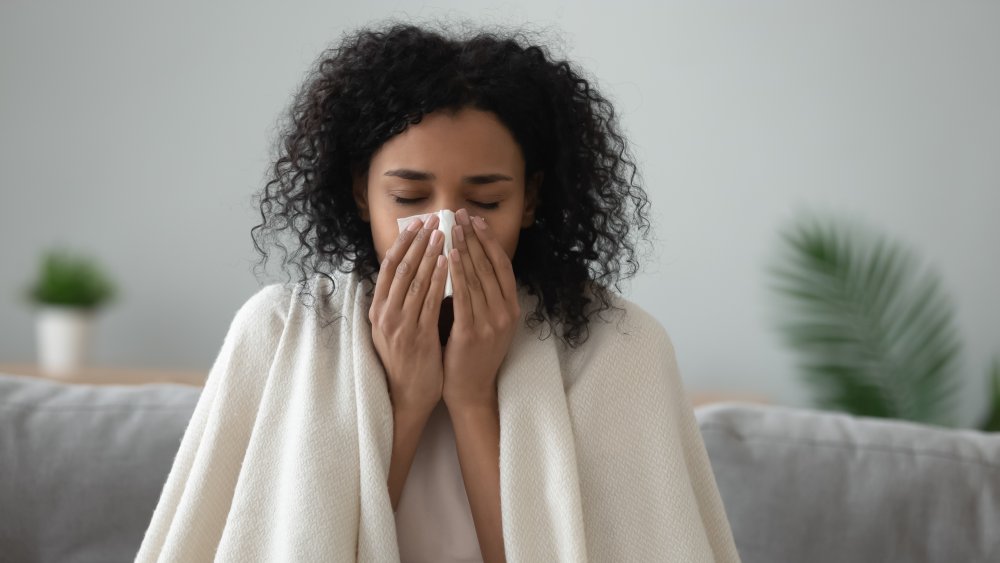 Ill Black young woman covered with blanket blowing running nose