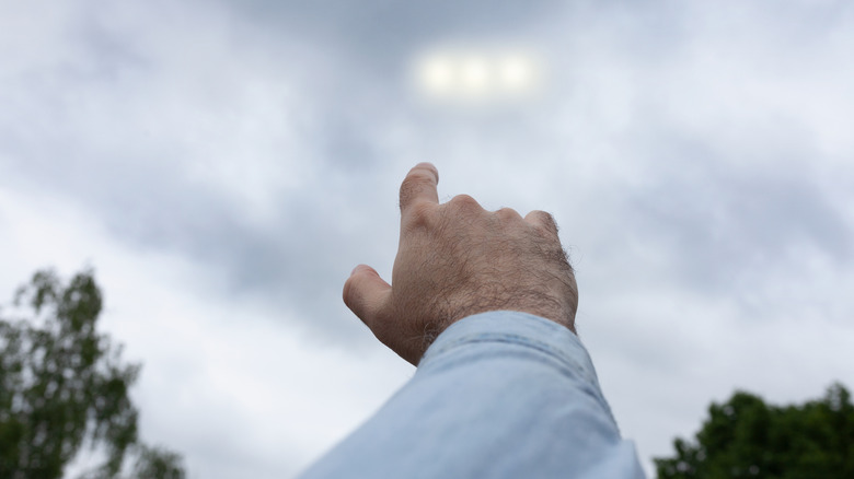 man's hand pointing at UFO lights in sky