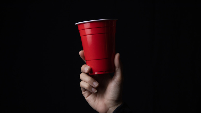 Hand holds up red Solo cup against black background