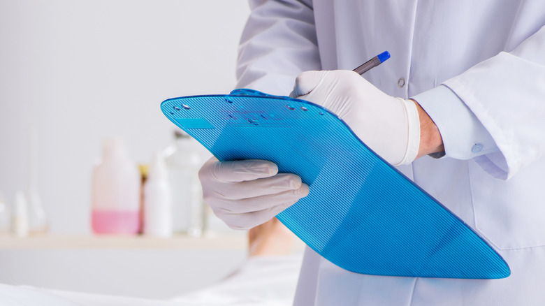 Closeup medical personnel with latex gloves writing on blue clipboard
