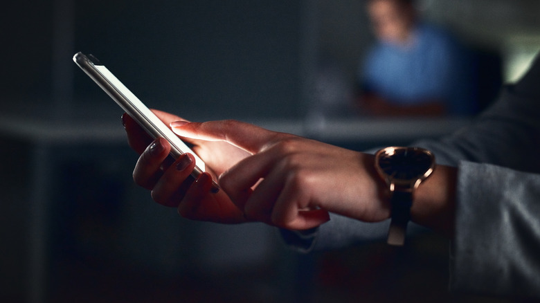 Closeup of person touching glowing phone screen in dark interior environment