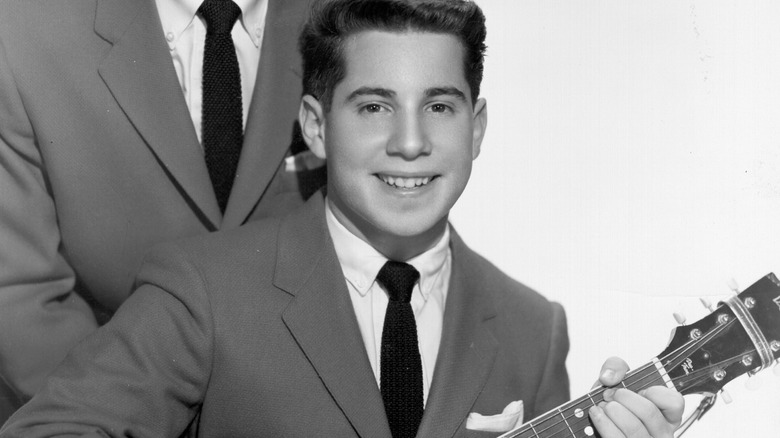 Young Paul Simon smiling with guitar in suit
