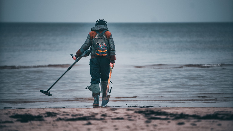 A man with a metal detector and a shovel at the beach
