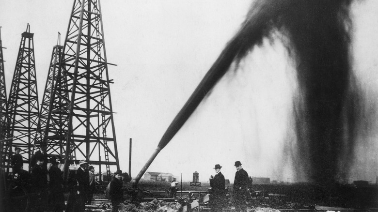 Vintage photo of men standing near oil gushing from pipe