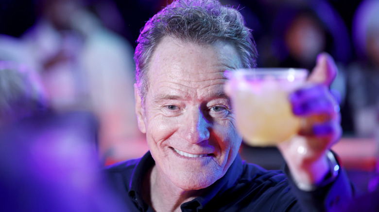 Bryan Cranston in a crowd smiling holding drink