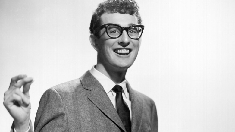 Buddy Holly in suit wearing glasses smiling and clicking fingers