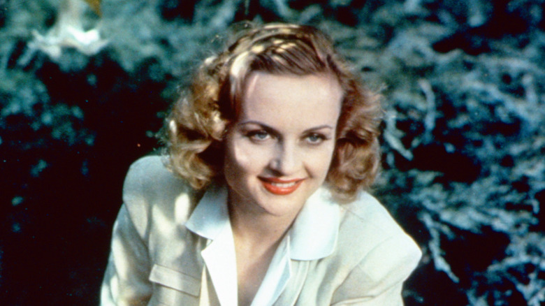 Carole Lombard posing in front of bushes and looking off