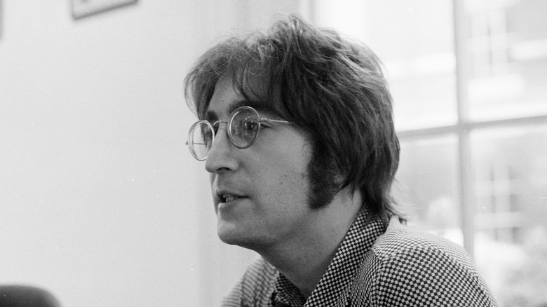 John Lennon with glasses in checkered shirt talking indoors
