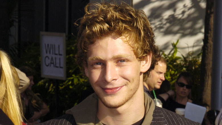 Johnny Lewis grinning in striped jacket outside with sun on face