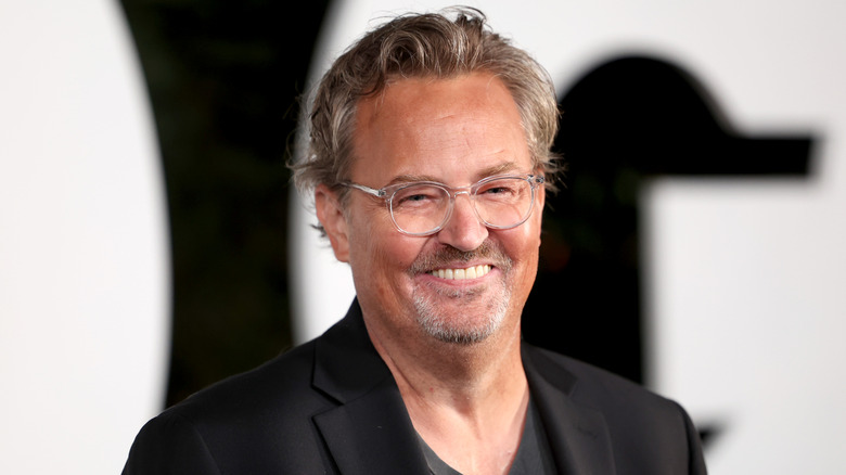 Matthew Perry smiling in glasses and suit at event