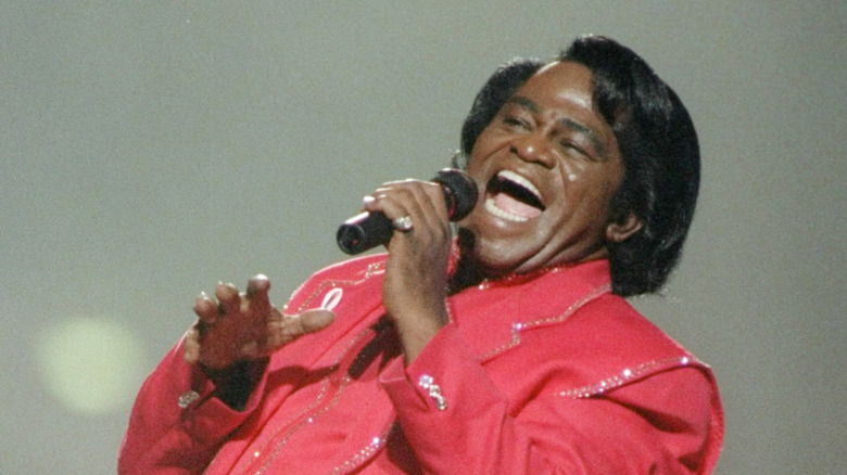 James Brown singing emphatically on stage in red suit