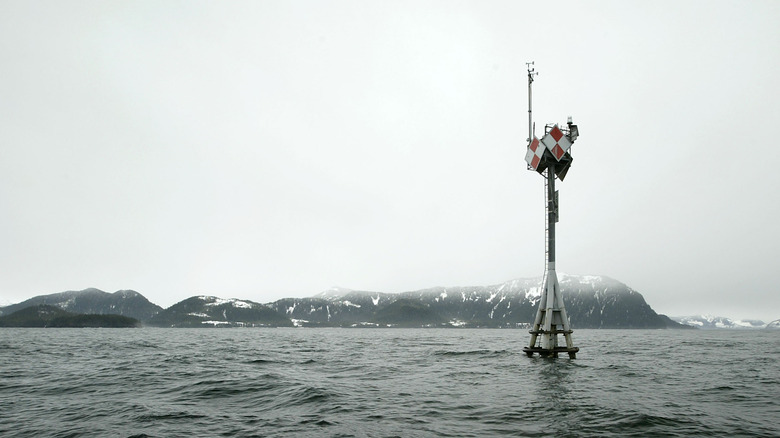 A pylon marking the location of the Exxon Valdez crash on Prince William Sound against a dreary, foggy craggy coastline.