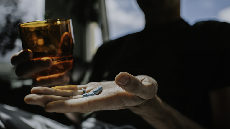 shadowy person with pills in one hand and a glass in the other