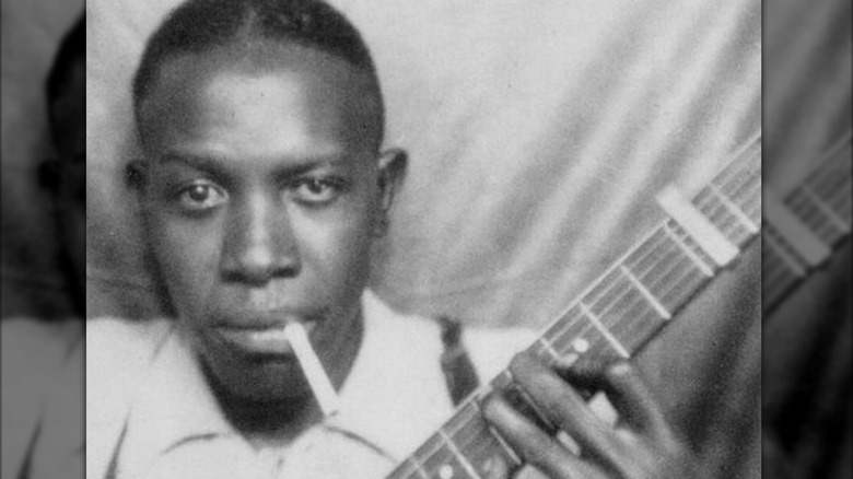 Legendary blues player Robert Johnson holding a guitar with a cigarette in his mouth