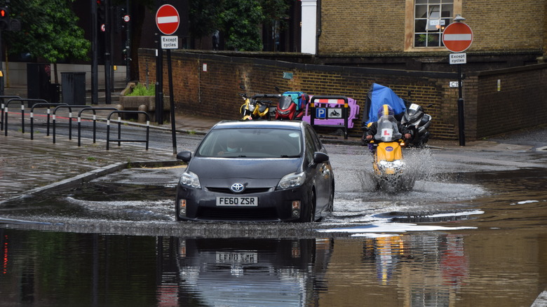 A car and a motorcycle driving through water on a flooded London street