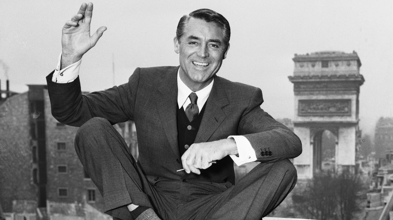 Carey Grant sat on tall building smiling in suit waving