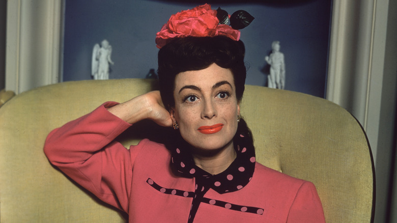 Joan Crawford sat smiling in pink suit and hat