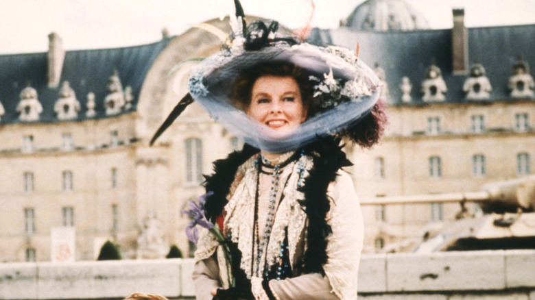 Katharine Hepburn smiling in giant hat outdoors by stately building