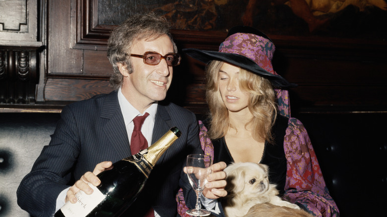 Peter Sellers sat smiling in suit pouring champagne