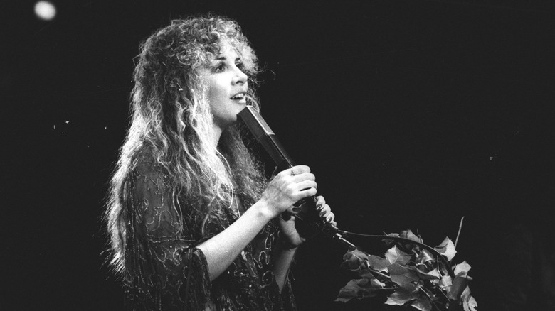 Stevie Nicks singing on stage by flowers