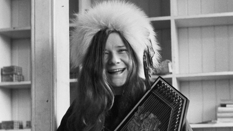 Janis Joplin sat smiling holding stringed instrument