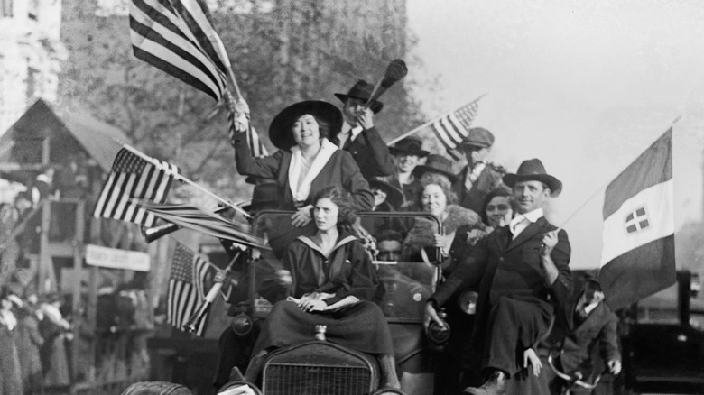 group on car waving american flags blowing horns armistice day