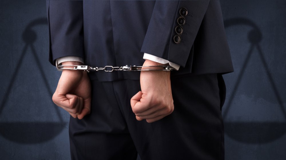 Arrested businessman in handcuffs with hands behind back and justice symbol wallpaper