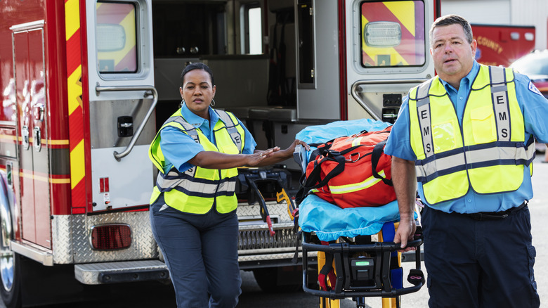 Two paramedics exit an ambulance with an empty gurney