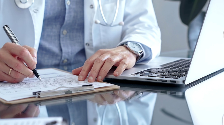 Doctor writing medical records on a glass desk with laptop