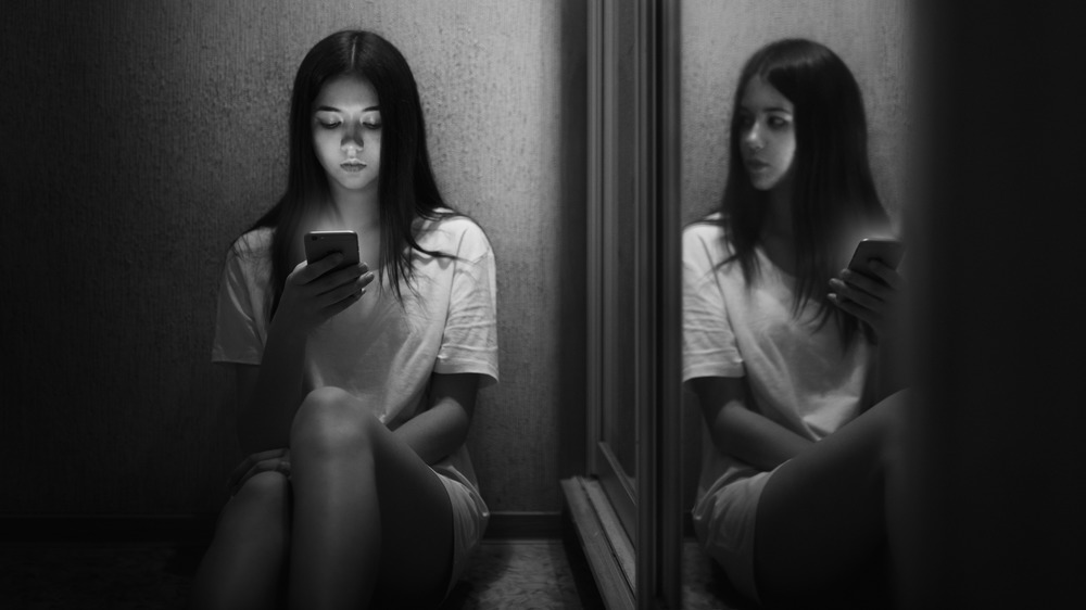Girls using phone while her reflection is turned toward her