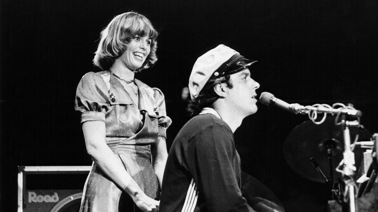 Toni Tennille smiling and Daryl Dragon wearing a boating cap playing piano on stage