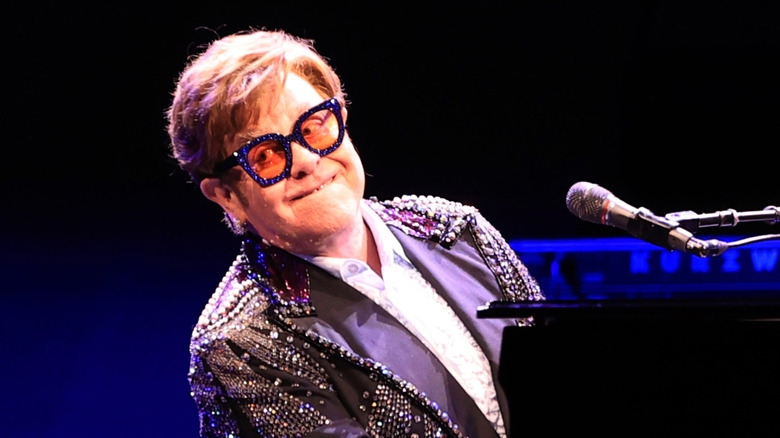 Elton John in glasses smiling at piano