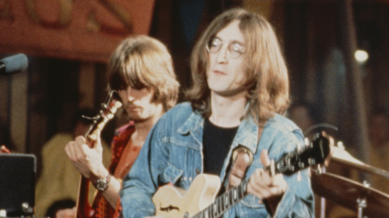 Eric Clapton plays guitar behind John Lennon playing guitar