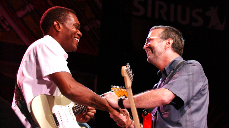 Robert Cray and Eric Clapton holding guitars and shaking hands and smiling