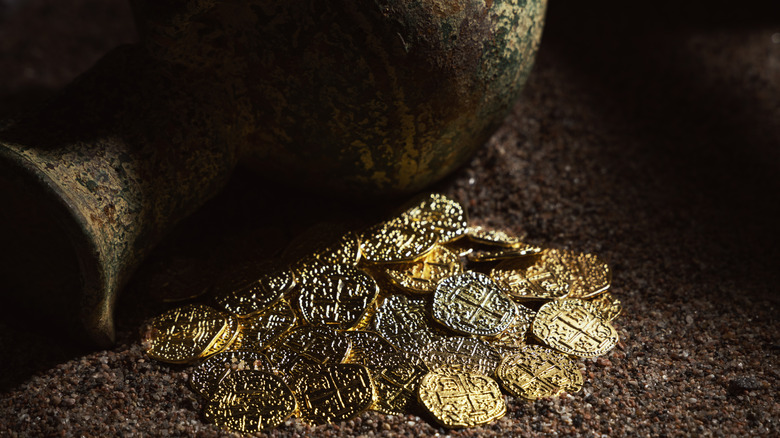 Jug with gold coins in sand